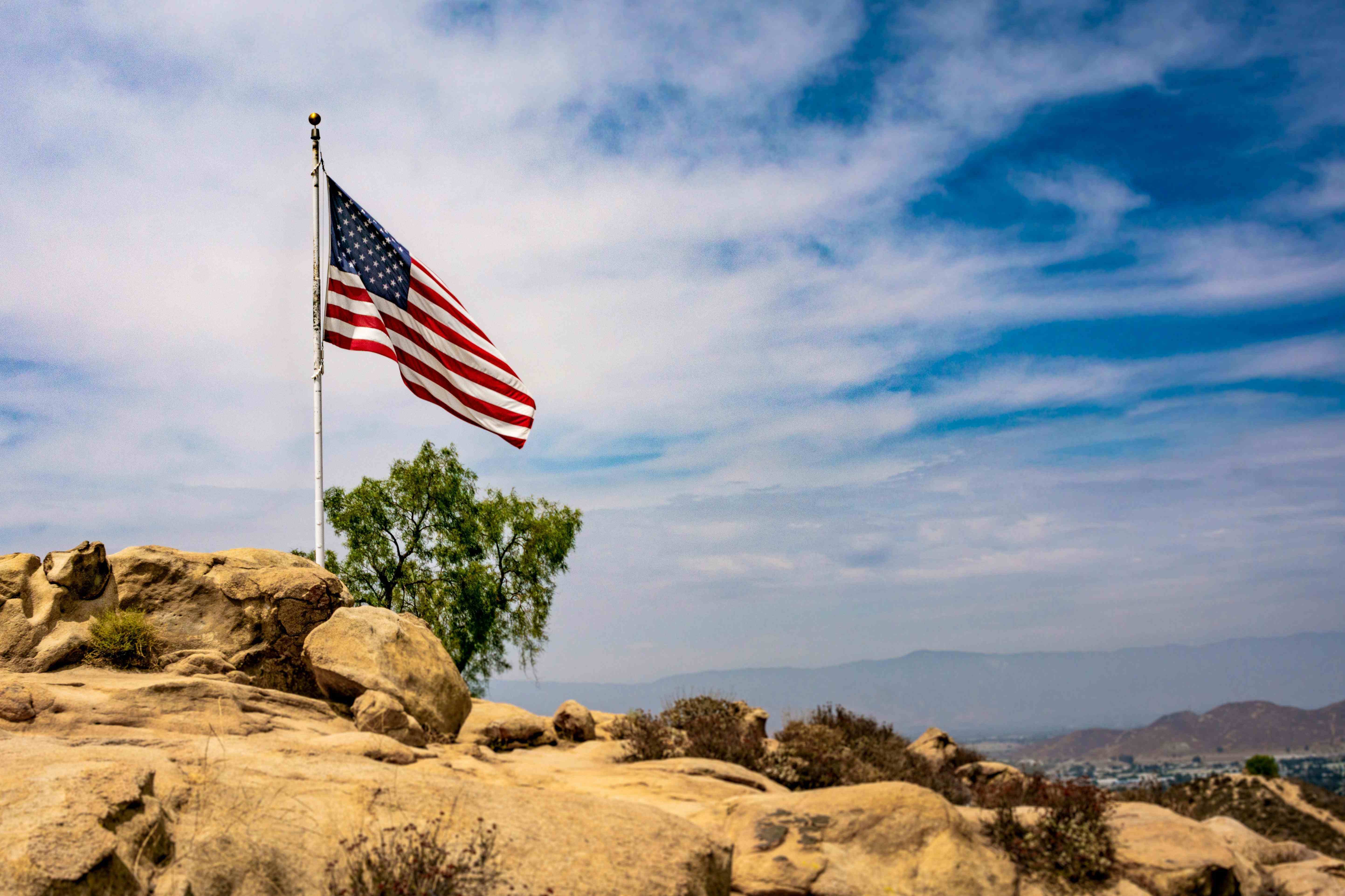 American flag standing proudly on rocky terrain with mountains in the distance